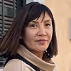 Portrait of a woman with shoulder-length dark hair wearing a beige coat outdoors.