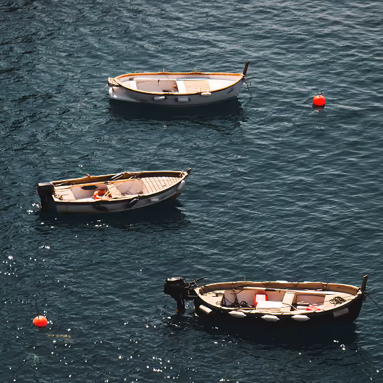 Three small boats floating on calm dark blue water near two red buoys.