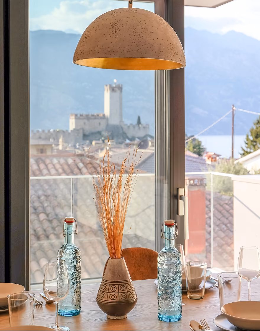 Balcony with table and chairs overlooking red tile roofs, a castle, and mountains in the distance.