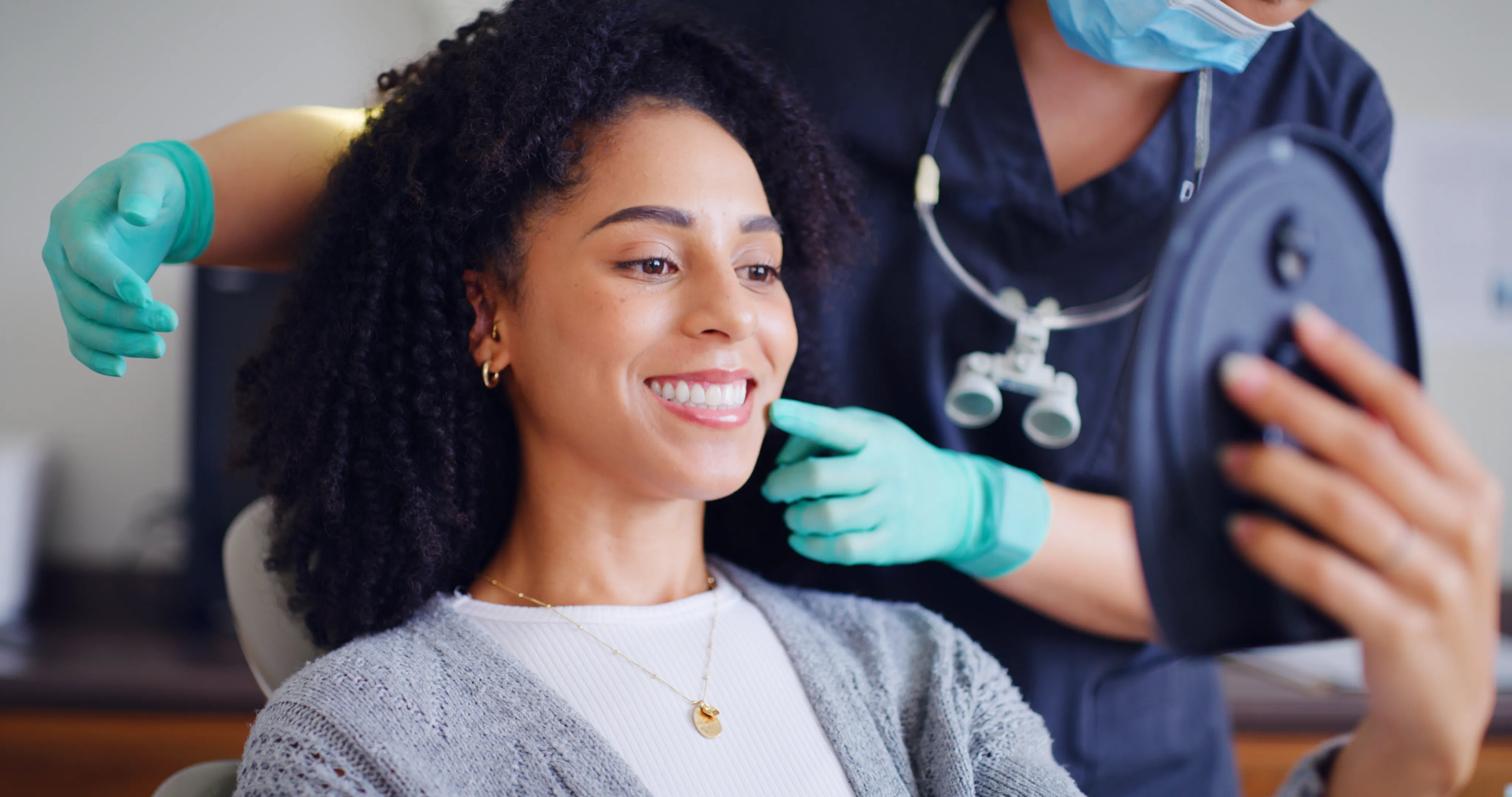 Dental professional pointing to a patient's smile as she checks it in a hand mirror