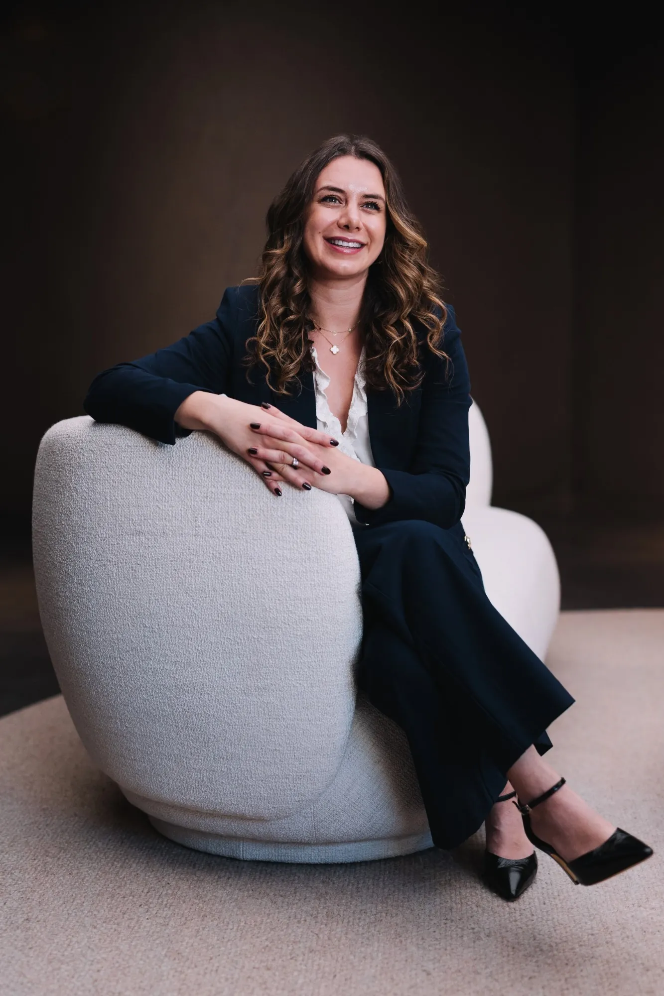Dr Payvand Menhadji, Specialist Periodontist, smiling and seated in a white armchair