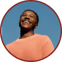 Smiling person in a coral sweater looking up against a clear blue sky.