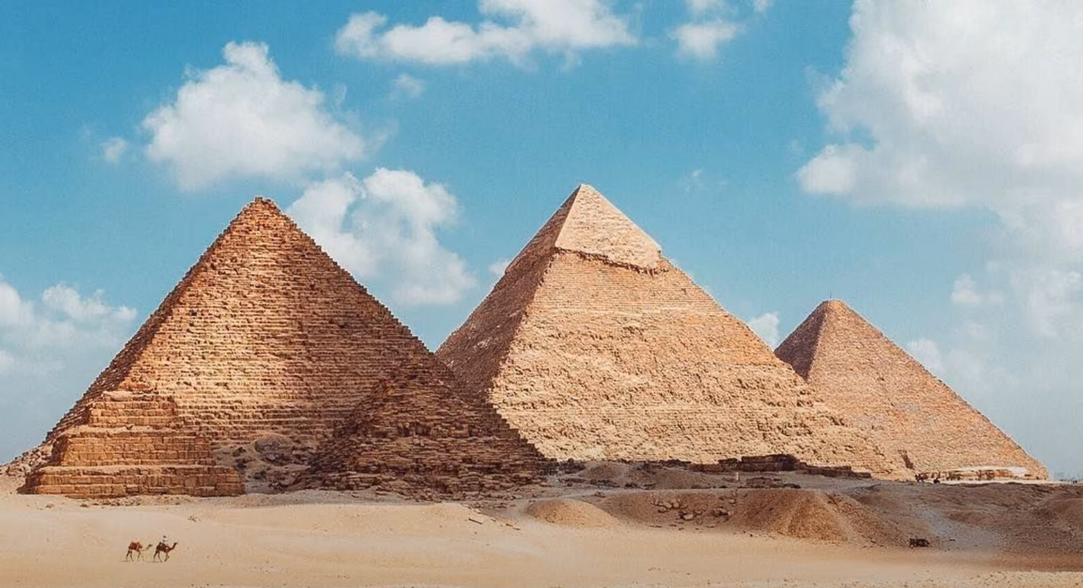 Three ancient Egyptian pyramids in desert under a blue sky with scattered clouds.