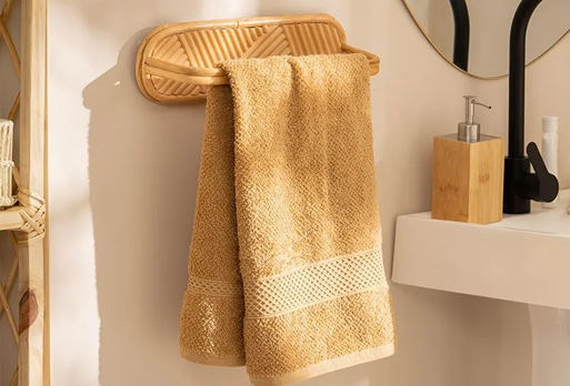 Toalla de mano color beige colgada en un soporte de pared de bambú junto a un lavabo con dispensador de jabón.