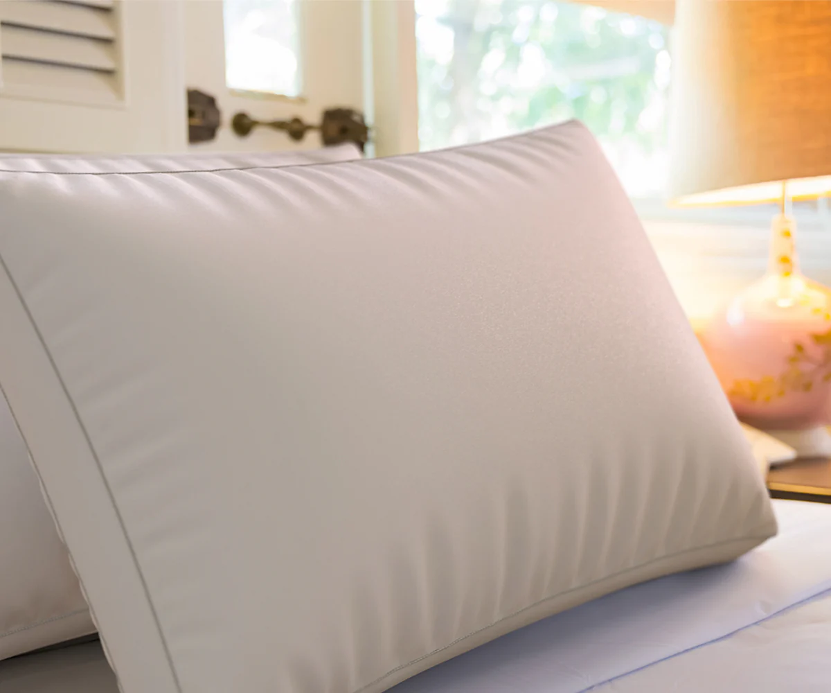 Almohada ajustable de espuma blanca sobre una cama con luz cálida de lámpara a un lado.