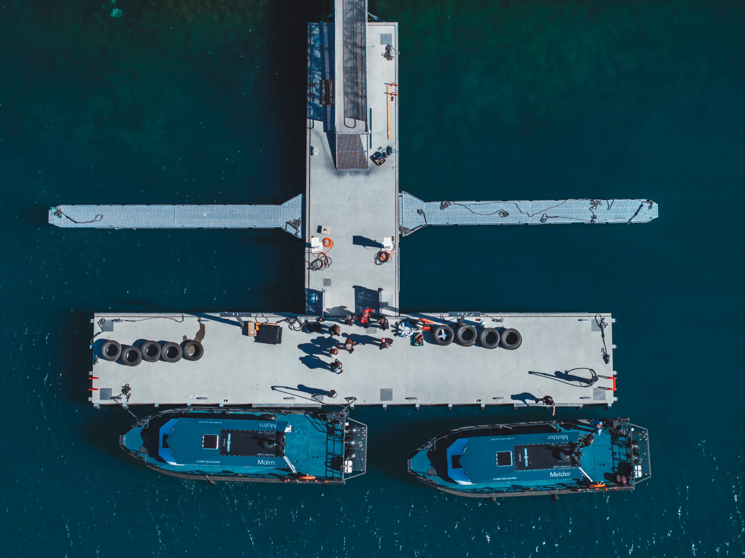 Aerial view of two electric boats docked at a pier with people standing on the pier.