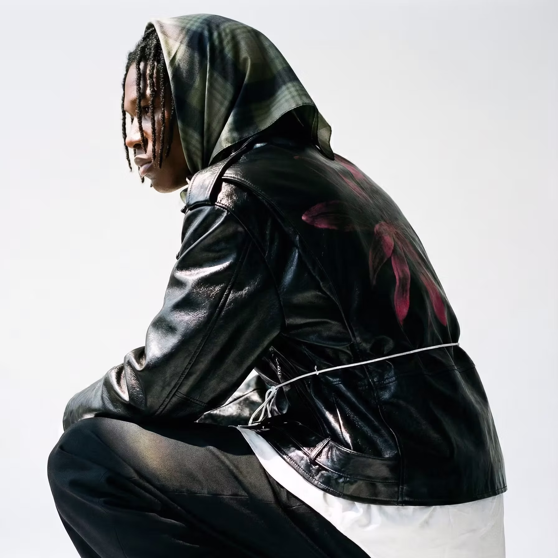Profile of person with braids wearing a hood and black leather jacket with pink flower on back.
