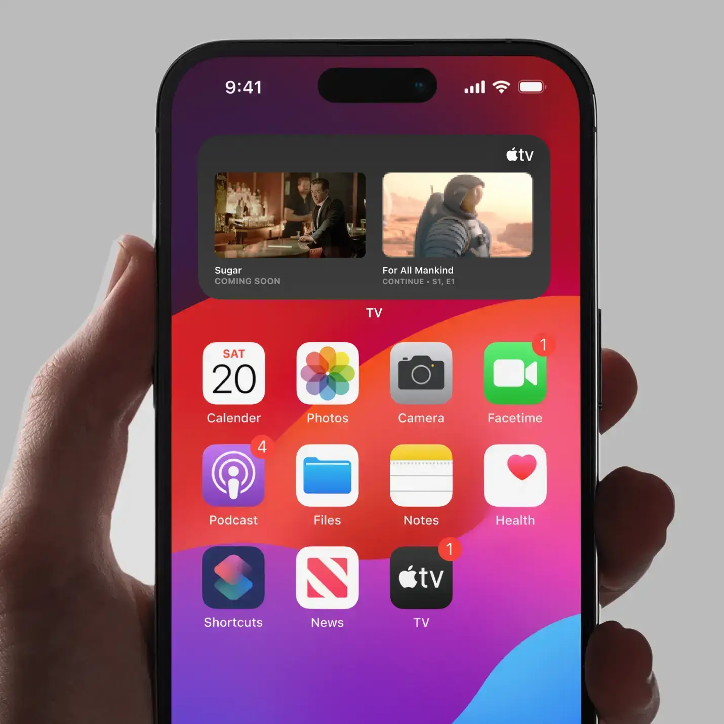 Hand holding an iPhone showing apps like Calendar, Photos, Podcasts, and Apple TV with watchlist widget.