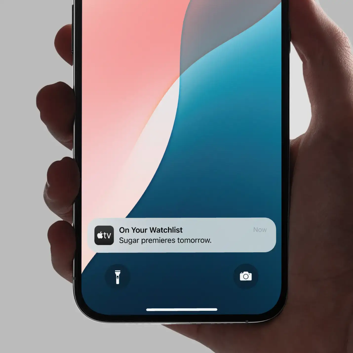 Hand holding smartphone displaying Apple TV notification: Sugar premieres tomorrow on your watchlist.