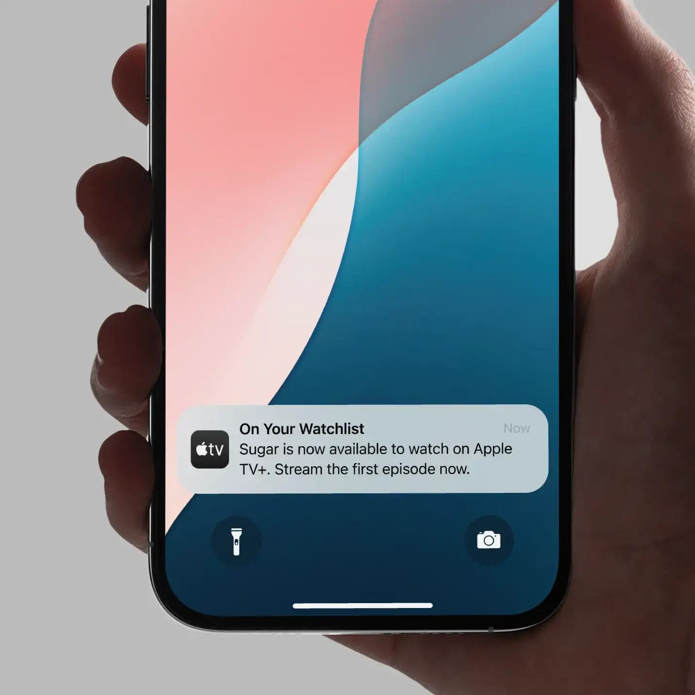 Hand holding iPhone showing Apple TV notification for new show Sugar available to stream.