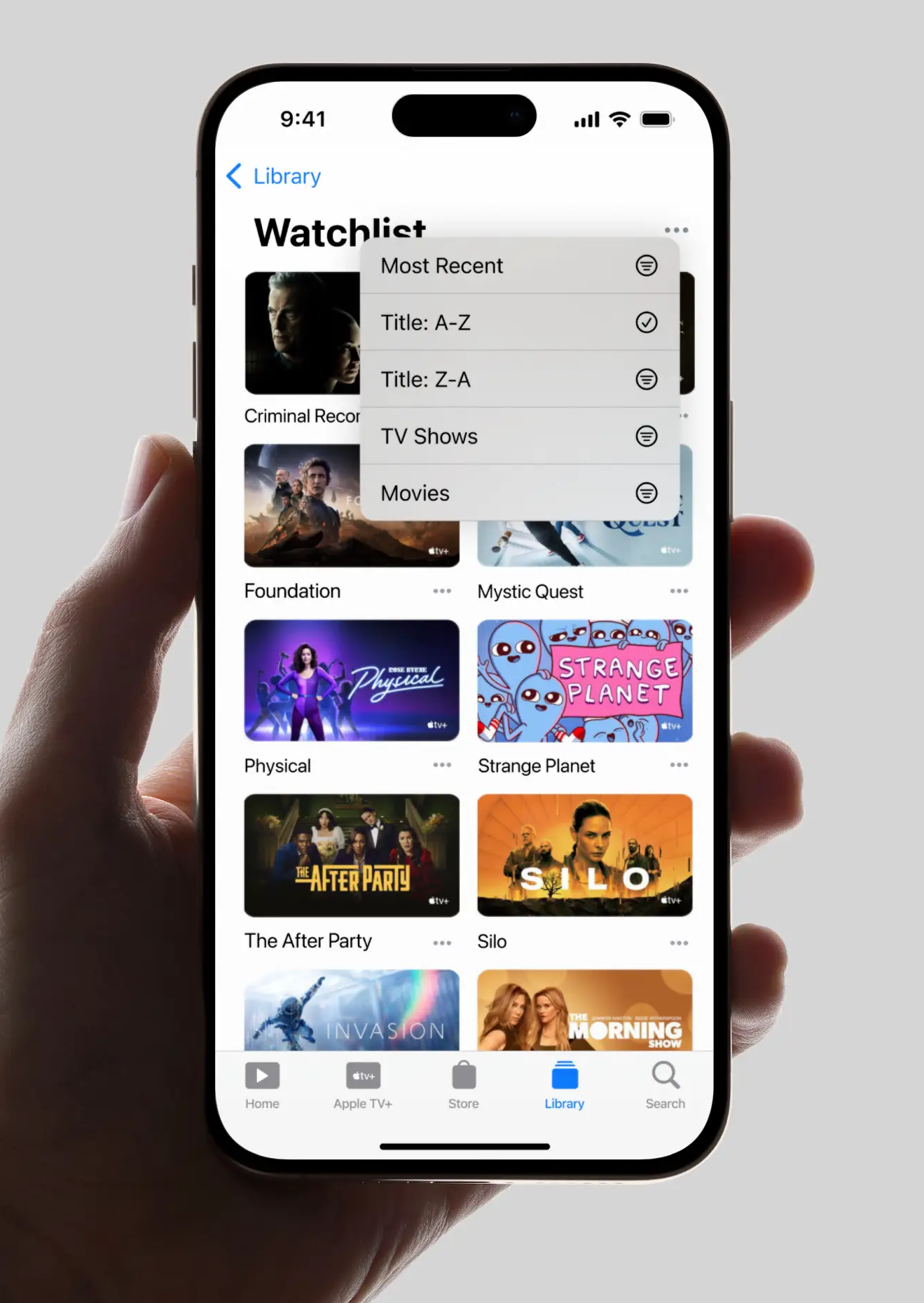 Hand holding phone showing Apple TV+ Watchlist sorted A-Z with thumbnails of various TV shows.