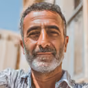 Portrait of a middle-aged man with salt-and-pepper hair and beard, outdoors with blurred background.