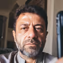 Middle-aged man with short curly hair and beard looking straight ahead indoors.