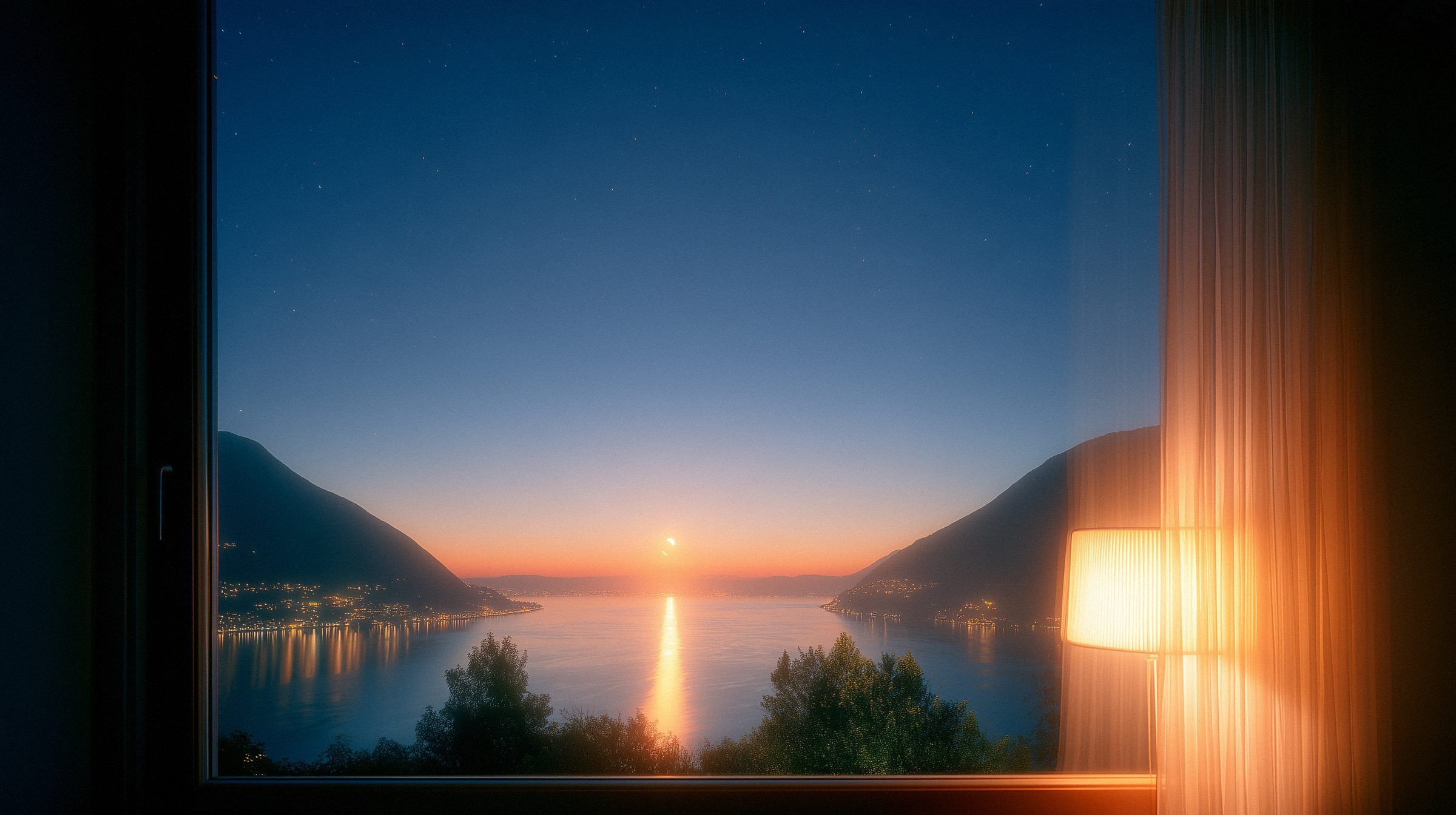 A lamp lit by a window over the lake at dusk