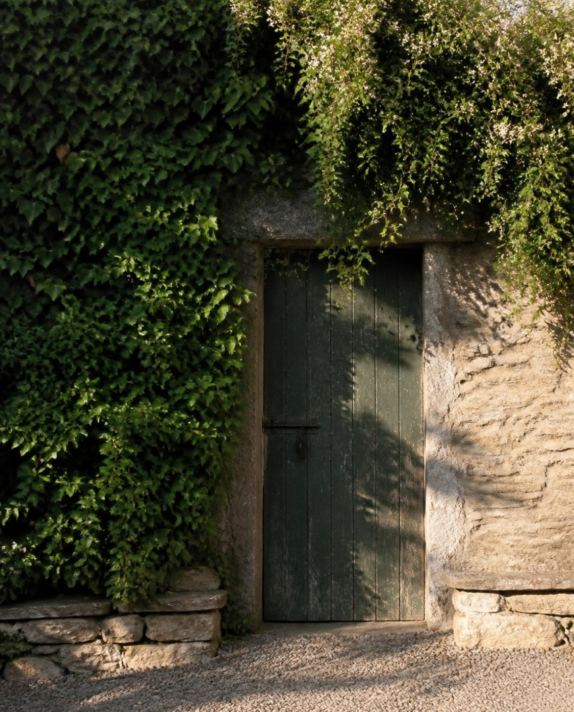 A closed wooden door in an old stone garden wall covered in ivy