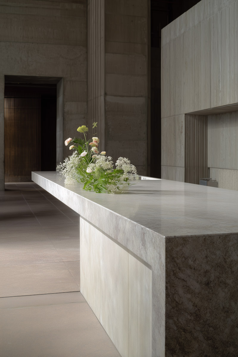 Modern white marble table with delicate flowers in a spacious room with stone walls and columns.