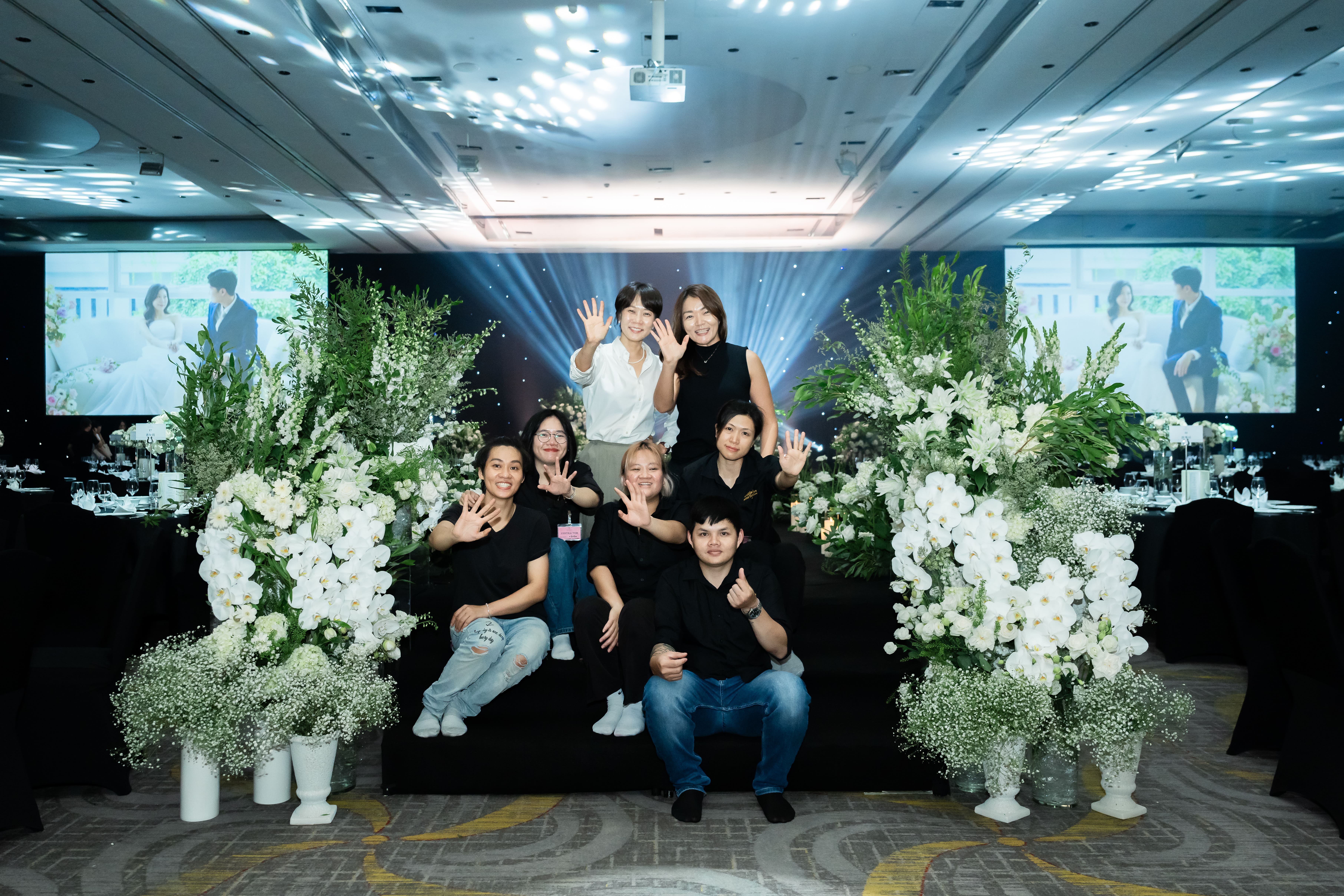 Team group photo posing beside white floral installations at event