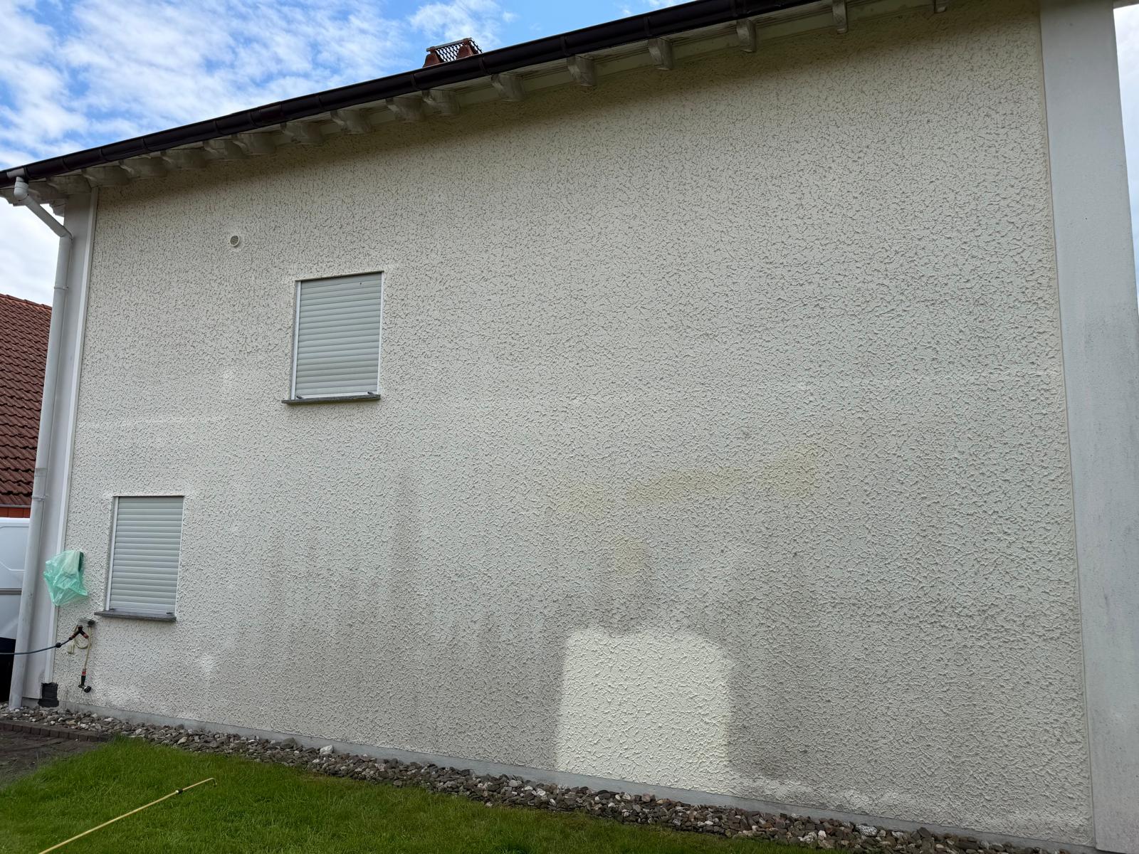 Exterior wall of a house with two closed windows and visible discoloration near the bottom half.