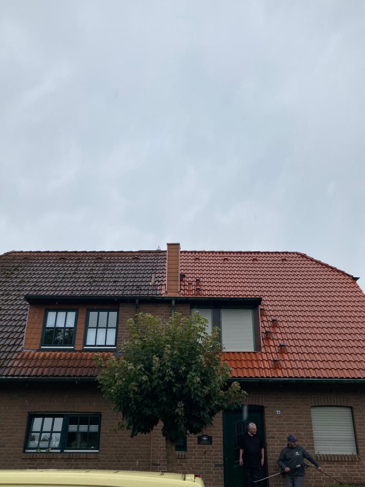 Brick house with brown and red tiled roof, a tree in front, two men outside near door on a rainy day.