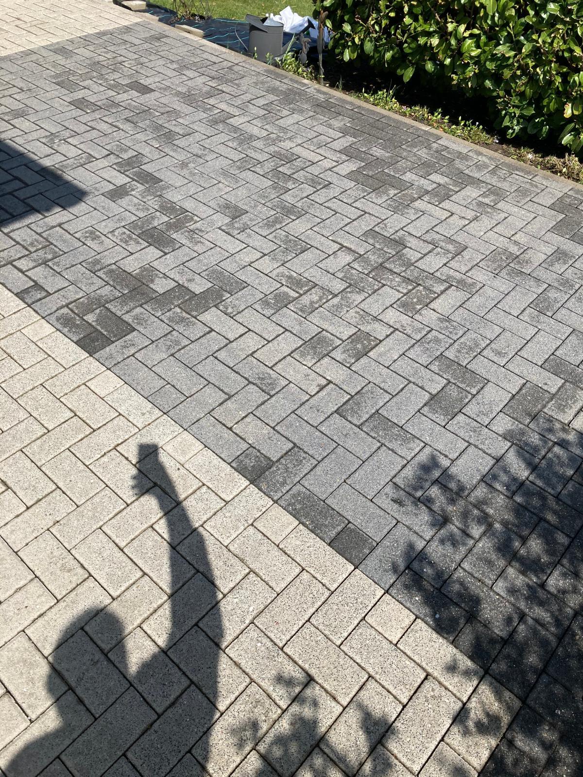 Light and dark gray herringbone stone pavement with shadow of person and nearby foliage.
