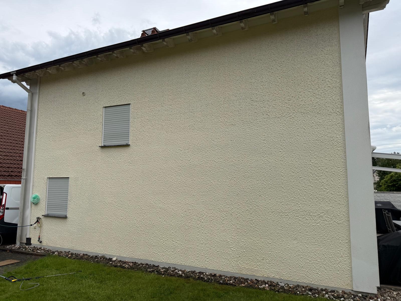 Side of a beige stucco house wall with two closed windows and a green lawn in front.