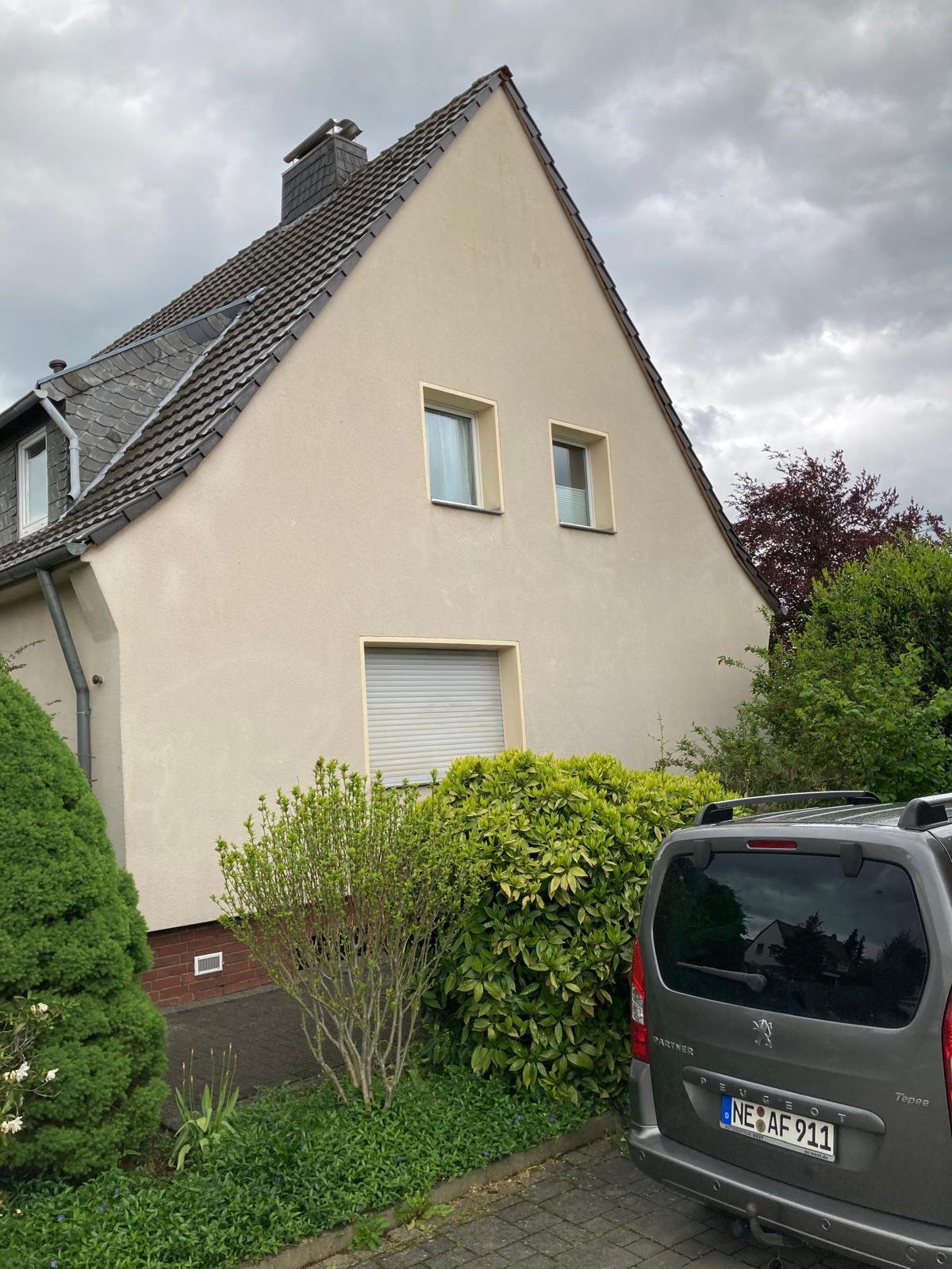Beige house with two upper windows, bushes in front, and a gray Peugeot car parked on driveway.