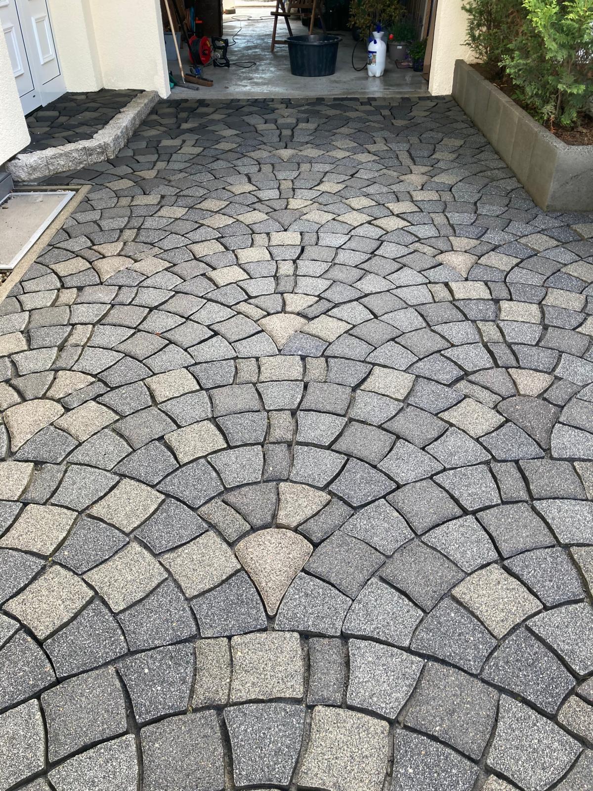 Stone driveway with a circular fan pattern in grey and beige tones leading to a garage entrance.