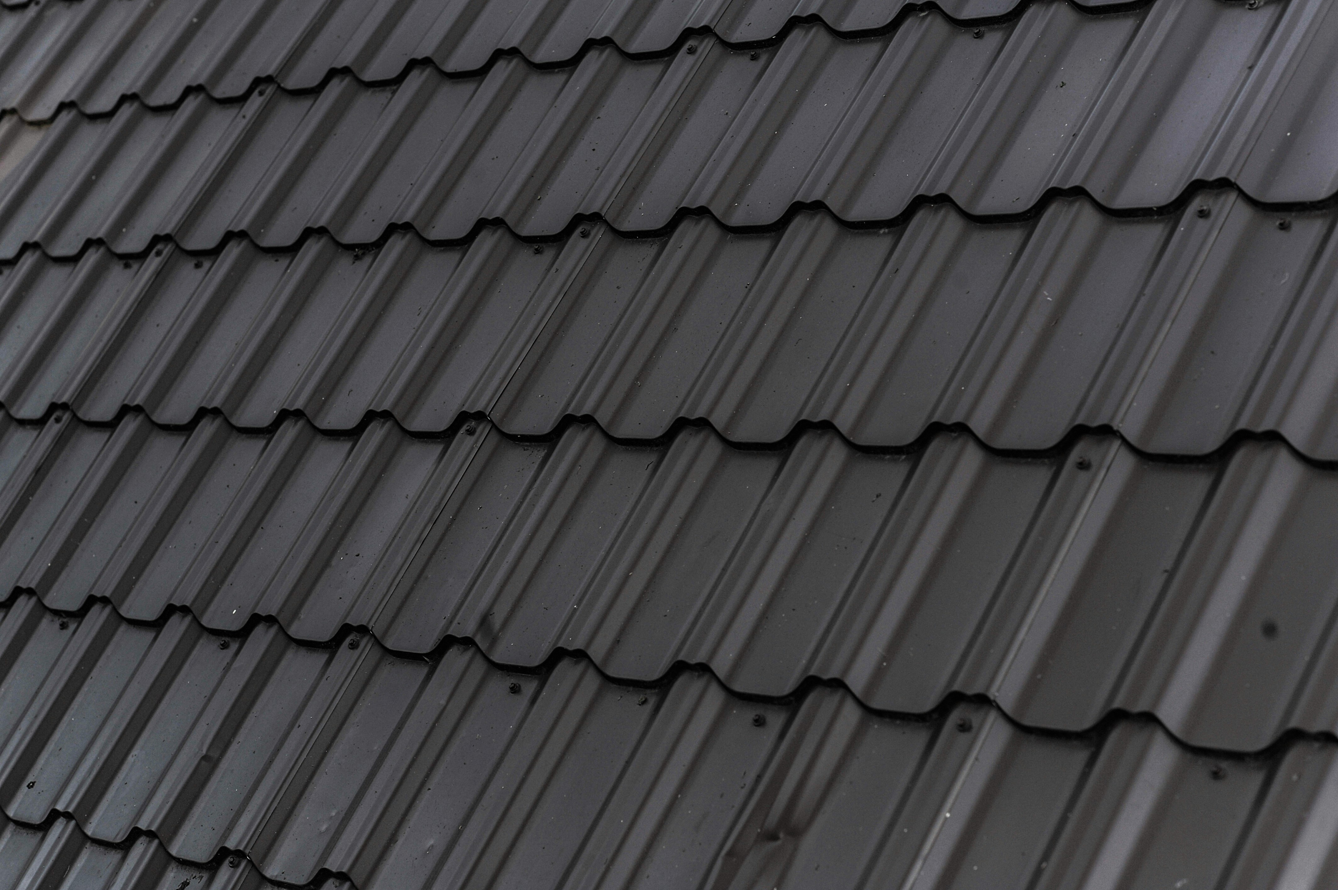 Close-up of dark gray metal roof tiles with a wavy pattern and vertical ridges, evenly arranged in overlapping rows.