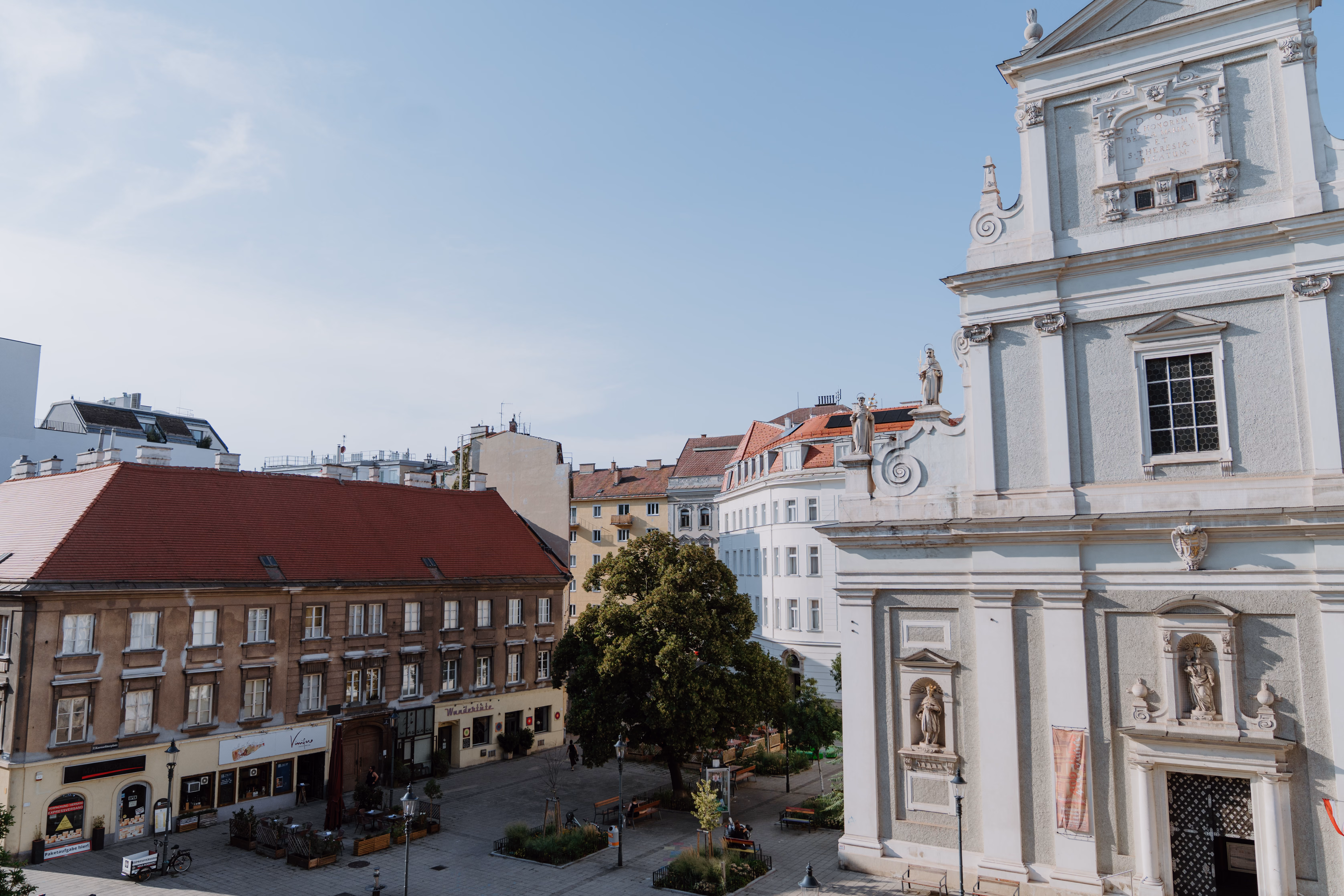 Straßenecke mit einem Gebäude, Bäumen, parkenden Lieferwagen und Schaufenstern eines Bekleidungsgeschäfts.
