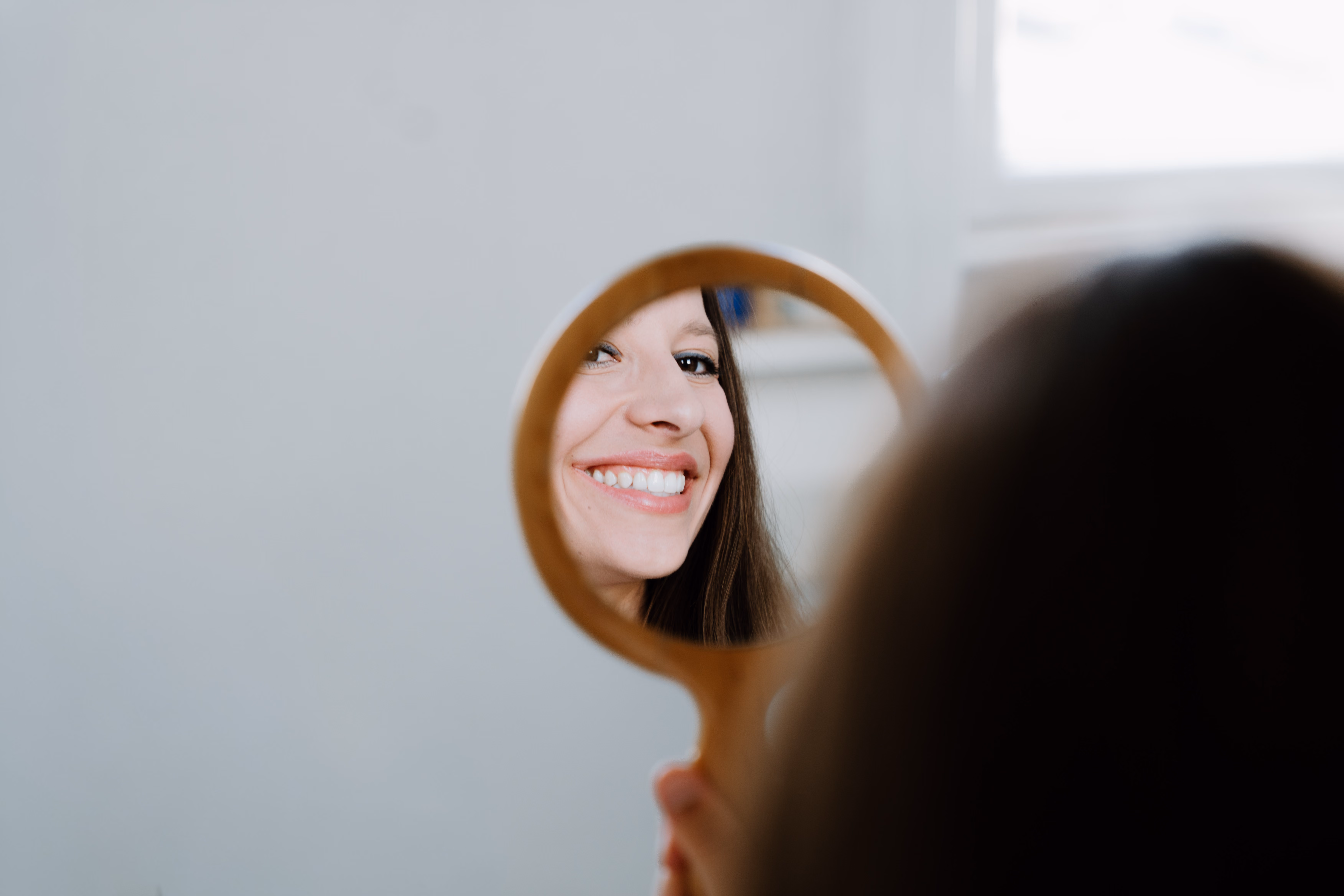 Frau lächelt und hält einen kleinen Handspiegel, der ihr Gesicht reflektiert.
