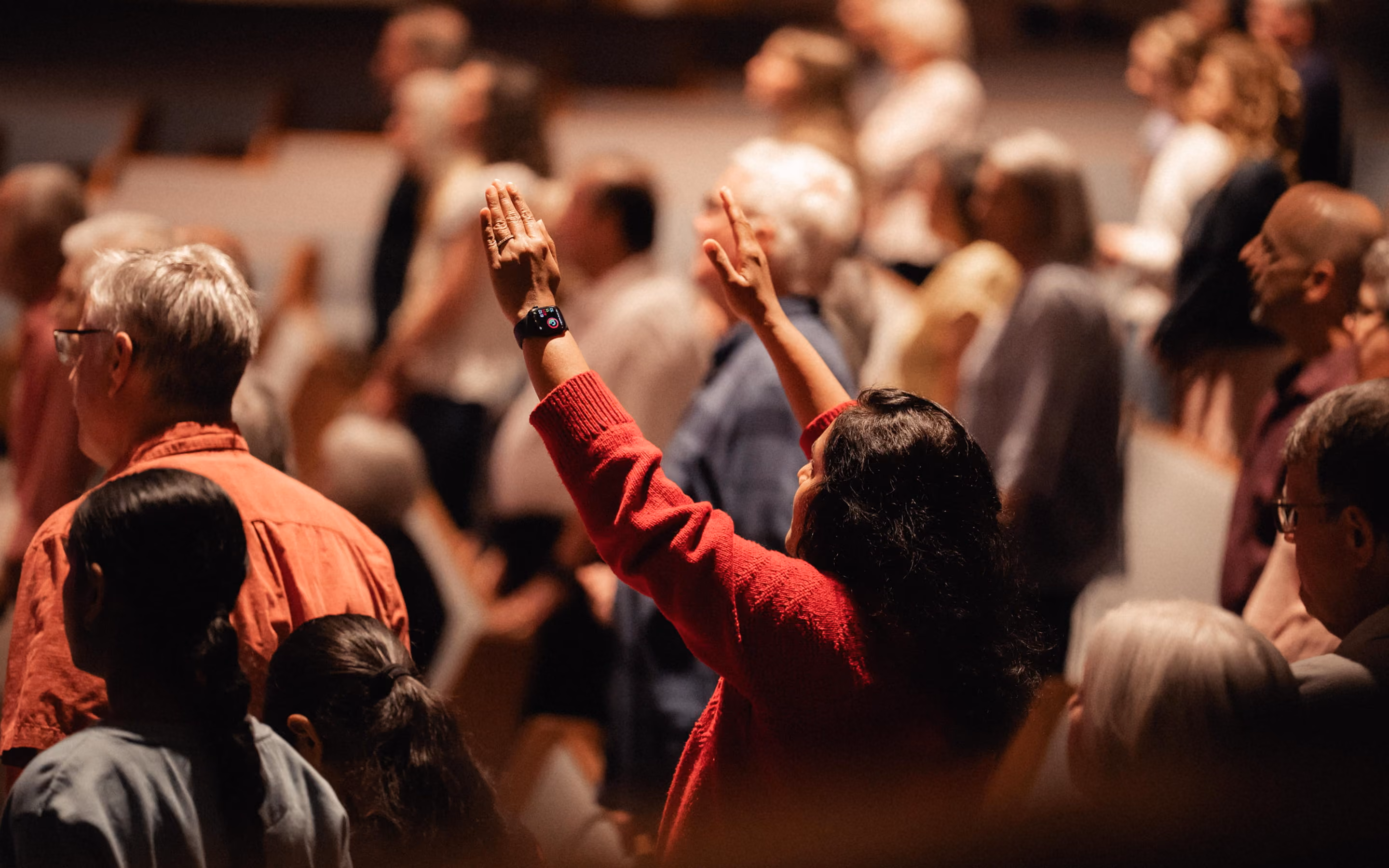 People gathered with one woman in a red sweater raising her hands, wearing a smartwatch.