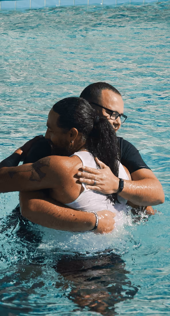Two people hugging in a swimming pool with water splashing around them.