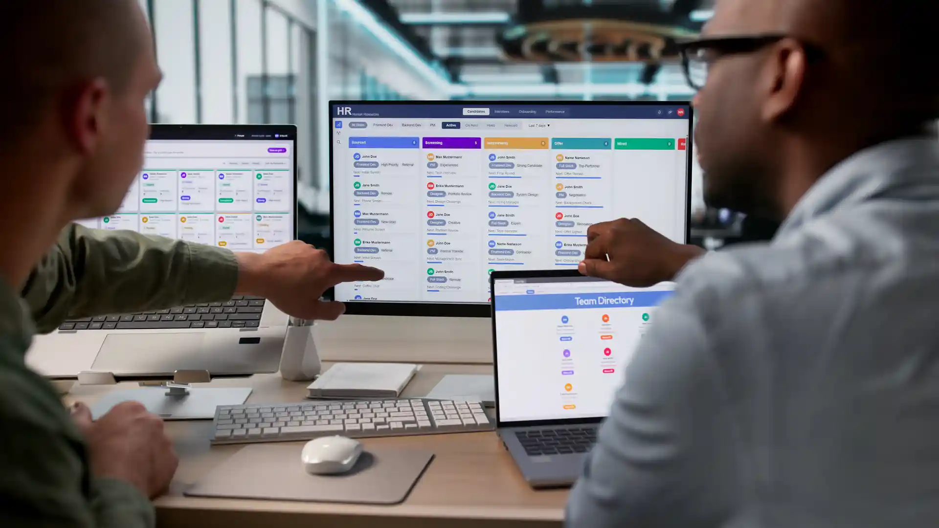 Two office workers sitting at a desk and viewing digital platforms on computer screens.
