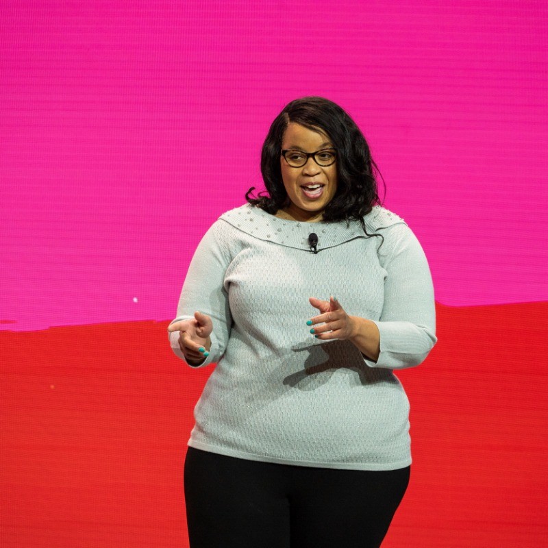 Photo of Nikki Wallace giving a talk about transforming education in front of a pink and red background