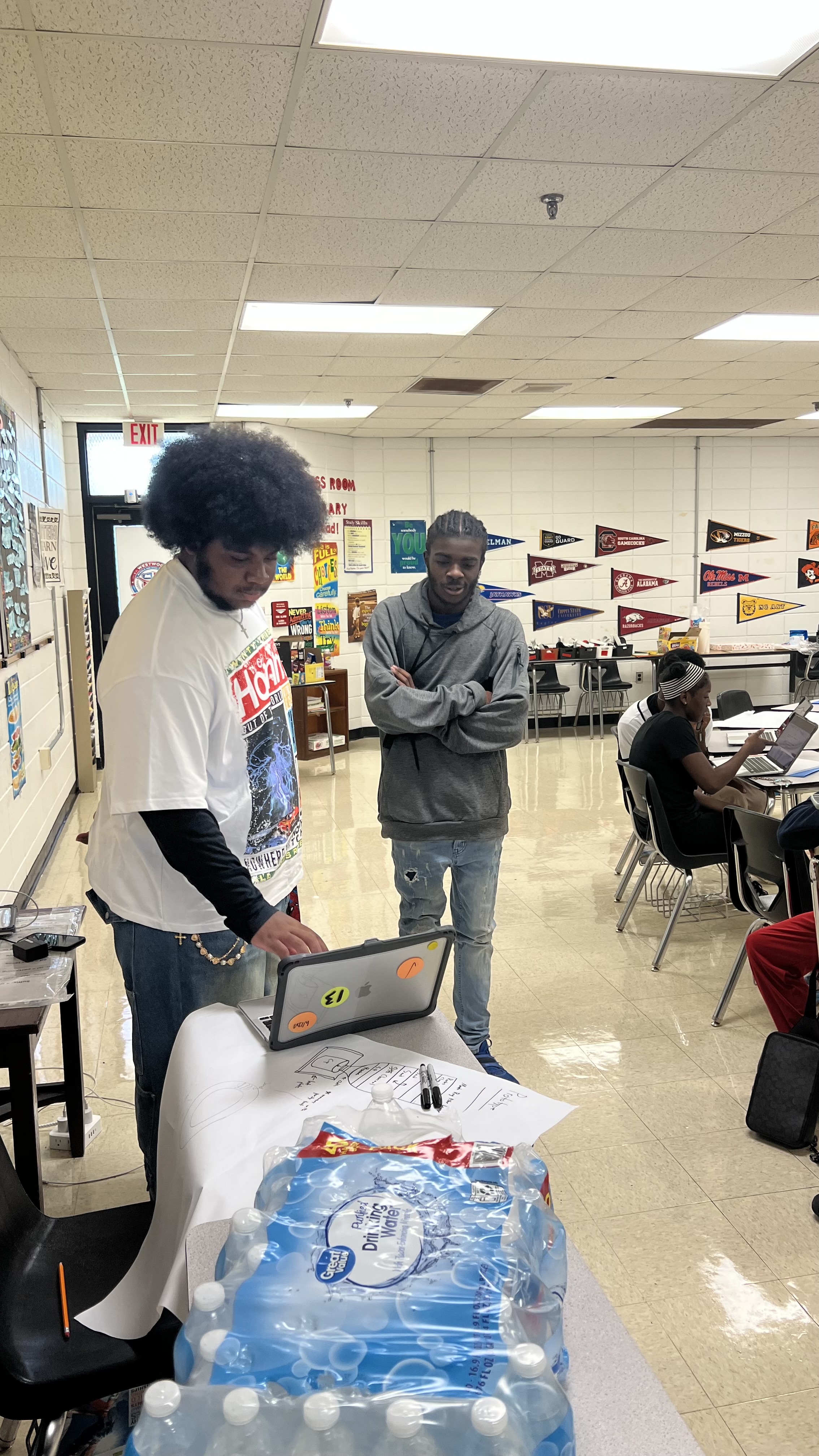 Two students looking at a laptop in front of a drawing of their prototype custom aquifer inspired by manta rays