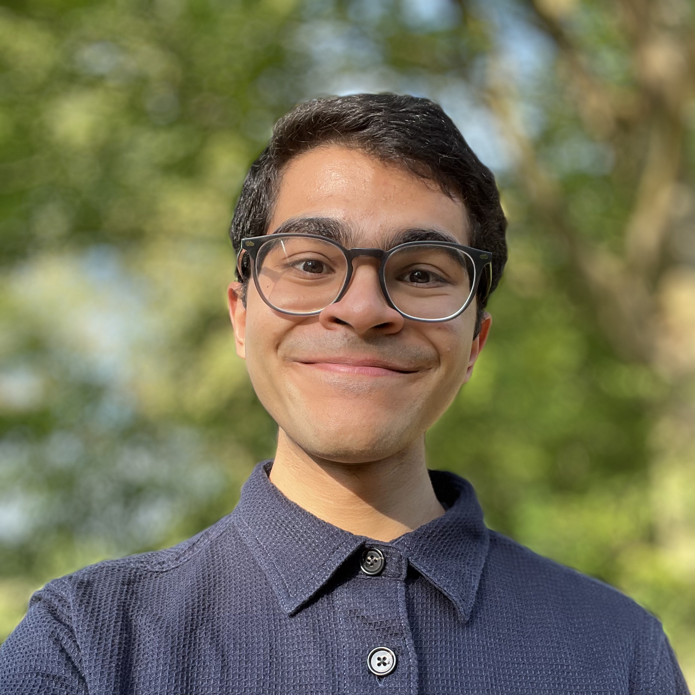 Headshot of Deep Thakkar with a blurred background of a tree behind him