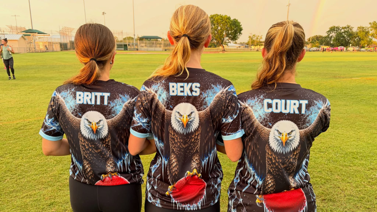 Three women standing with backs showing matching shirts with eagle and football, labeled Britt, Beks, Court.