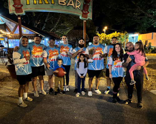 Group of people at night wearing matching Rollin' Buns shirts posing under tiki bar sign.
