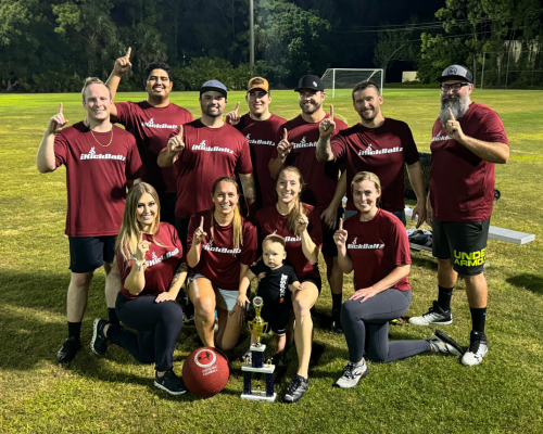Group of people posing on a field under lights, holding a trophy and celebrating a sports win.