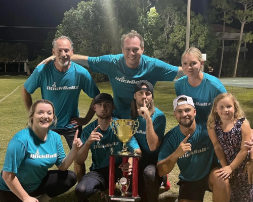 Group of nine people in green shirts holding a large trophy on a sports field at night.