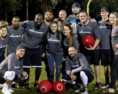 Group of people wearing blue KickBallz shirts sitting at tables in a casual indoor setting with drinks.