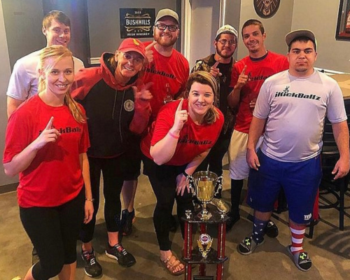 Group of people wearing blue KickBallz shirts sitting at tables in a casual indoor setting with drinks.