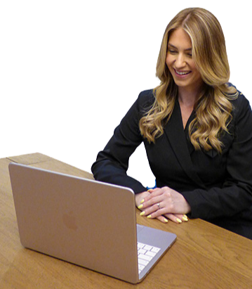 Smiling woman with long blonde hair sitting at table using a laptop computer.
