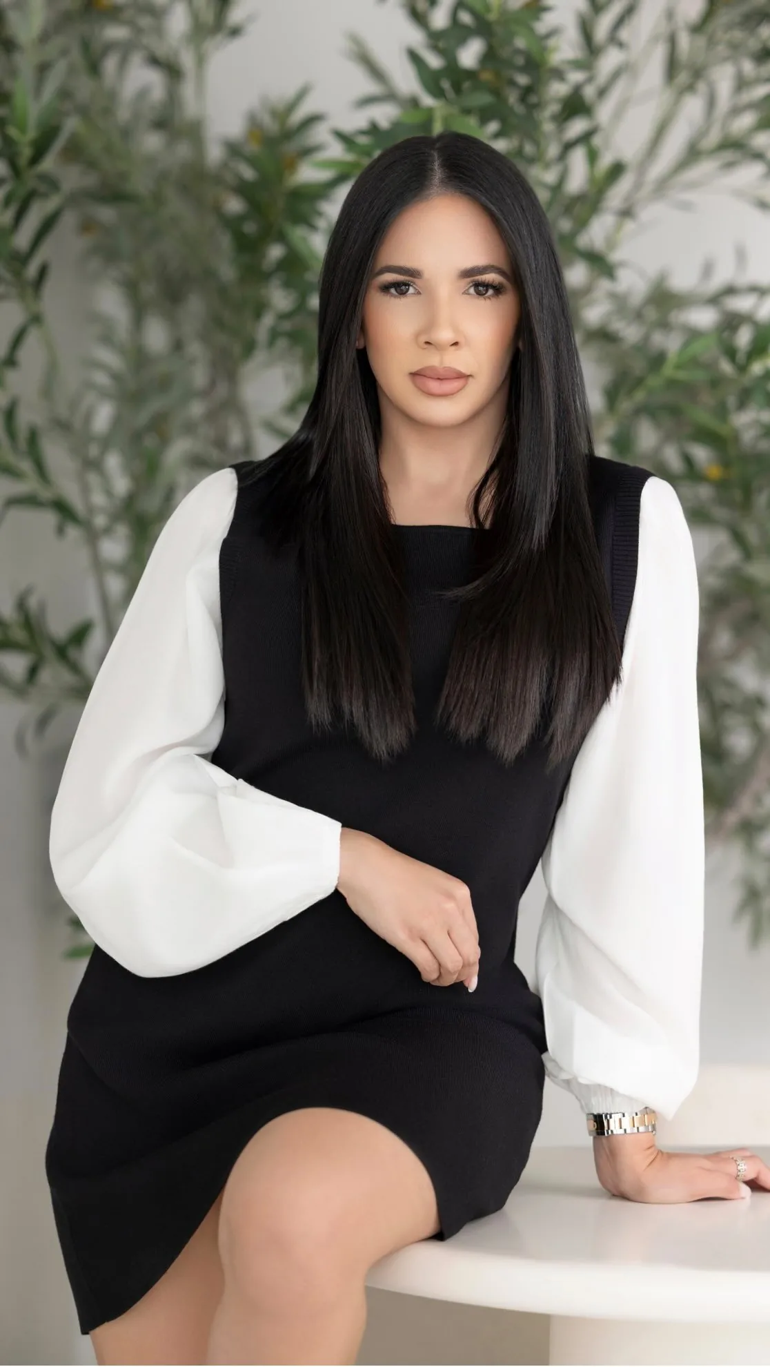 Woman with long black hair wearing black dress with white sleeves sitting on a white table.