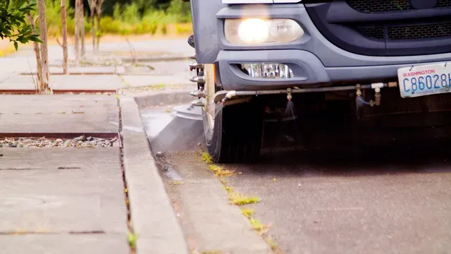 Sweeper truck spraying and sweeping along a curb