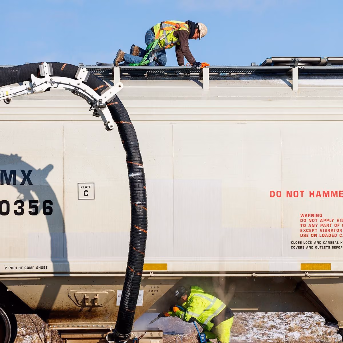 Crew cleaning a railcar with a vacuum hose from the top hatch