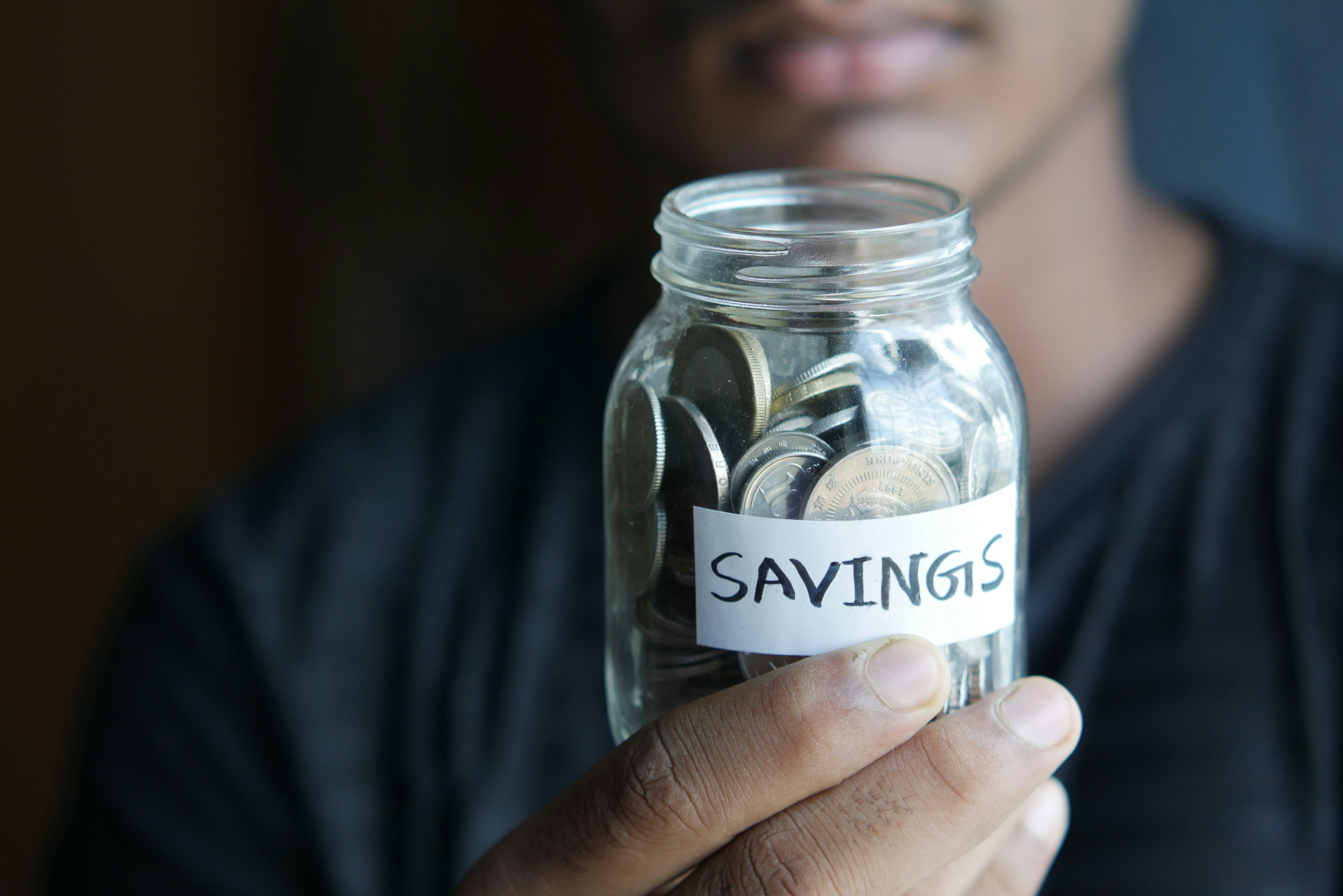 Hand holding a savings jar labeled Savings, filled with coins