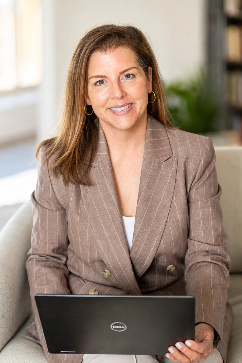 Kristin Moore in a taupe pinstripe blazer with a laptop, seated in a bright office. Founder of Growth Studio.