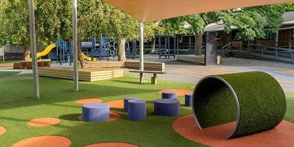 Playground with artificial turf, shade sail, stump seats and a turf-covered crawl tunnel