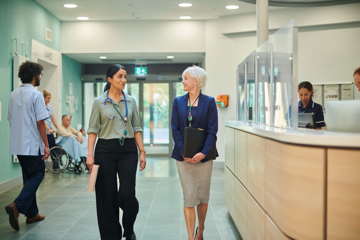 Clinician and hospital executive walking and talking in a hospital corridor near reception